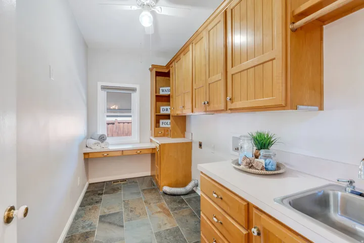 Functional utility room featuring natural wood cabinetry, a built-in sink with a countertop, slate tile flooring, and a window with a built-in desk