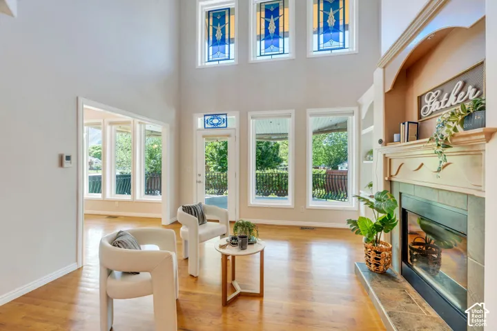 Two-story living area featuring high ceilings, wood-finish flooring, a fireplace with a tiled hearth and mantel, and multiple windows