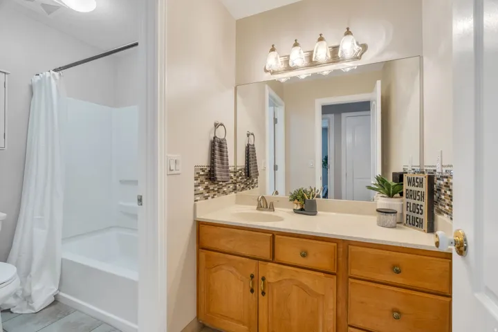 Vanity area featuring a light-toned countertop, wood-finish cabinetry with brass hardware, and a mosaic tile backsplash
