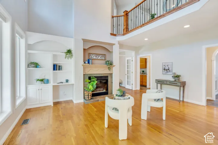 Two-story living area featuring wood-finish flooring, a fireplace with a mantel, built-in shelving, a second-story balcony with metal and wood railings, and white French doors