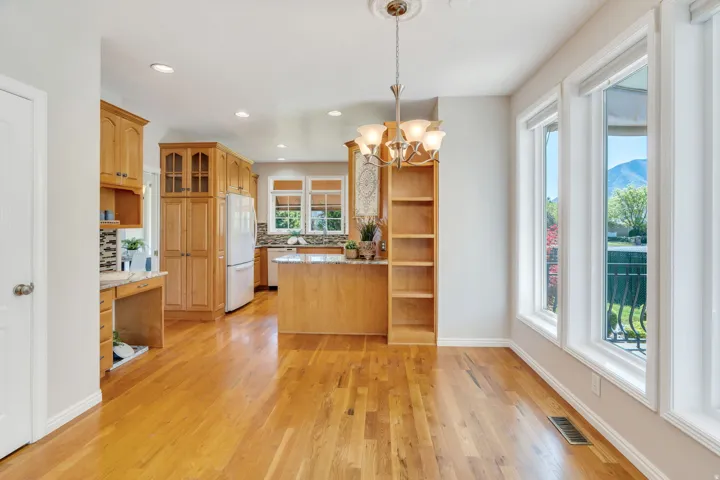 Open-concept kitchen and dining area featuring hardwood flooring, white appliances, light wood cabinetry, and a kitchen island with stone countertops