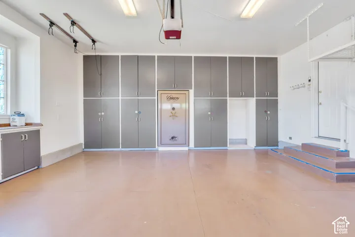 Spacious garage featuring extensive built-in cabinetry, durable flooring, a window, integrated overhead storage racks, and a garage door opener