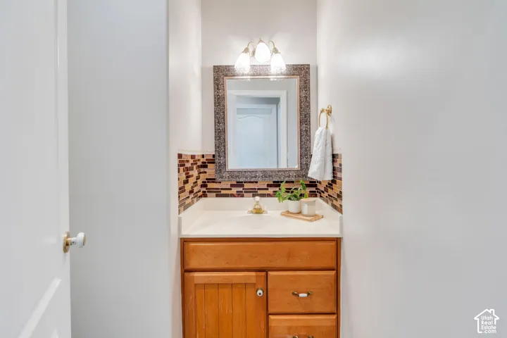 Vanity featuring a light wood-finish cabinet with paneling and drawers, a light-toned countertop, and a mosaic tile backsplash