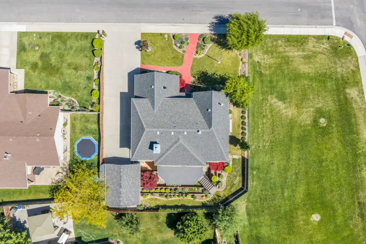 Aerial view showcasing a property with a grey shingle roof, paved driveway, and established landscaping