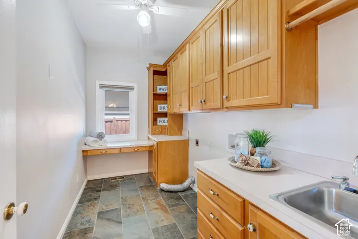 Functional utility room featuring natural wood cabinetry, a built-in sink with a countertop, slate tile flooring, and a window with a built-in desk
