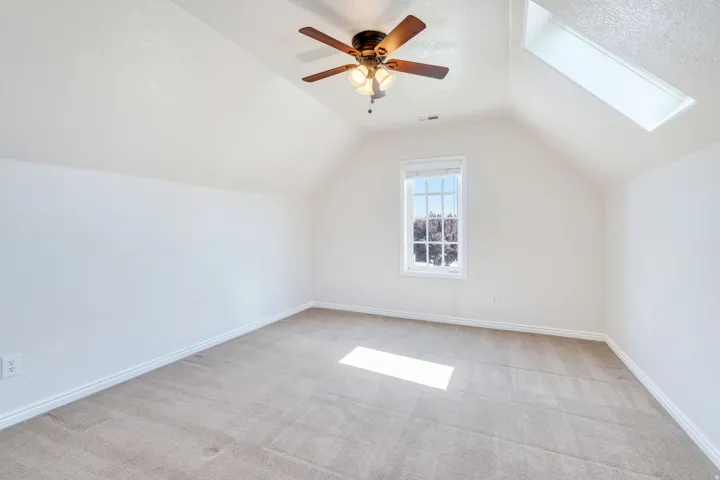 Room featuring a vaulted ceiling, a skylight, a window with exterior views, a ceiling fan with integrated lighting, and carpet flooring