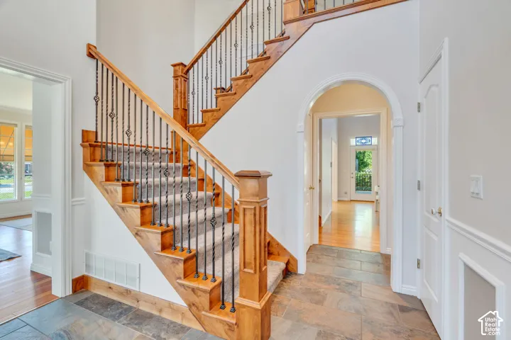 Grand staircase featuring natural wood newel posts, handrails, and treads with black wrought iron balusters and carpeted runners