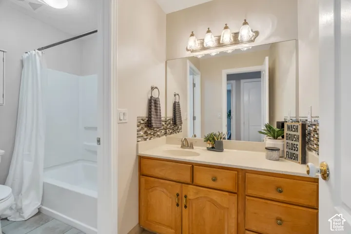 Vanity area featuring a light-toned countertop, wood-finish cabinetry with brass hardware, and a mosaic tile backsplash