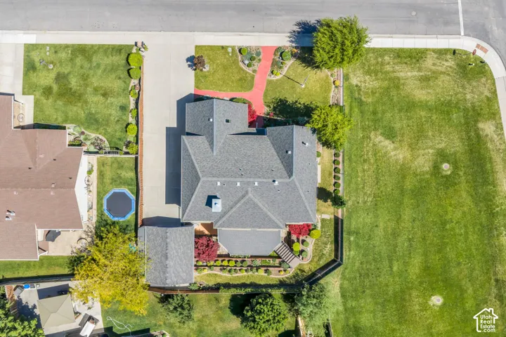 Aerial view showcasing a property with a grey shingle roof, paved driveway, and established landscaping