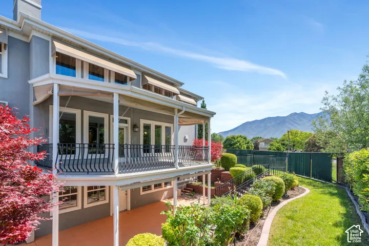 Multi-level exterior featuring a covered balcony with wrought iron railing, upper-level retractable awnings, and a lower-level patio