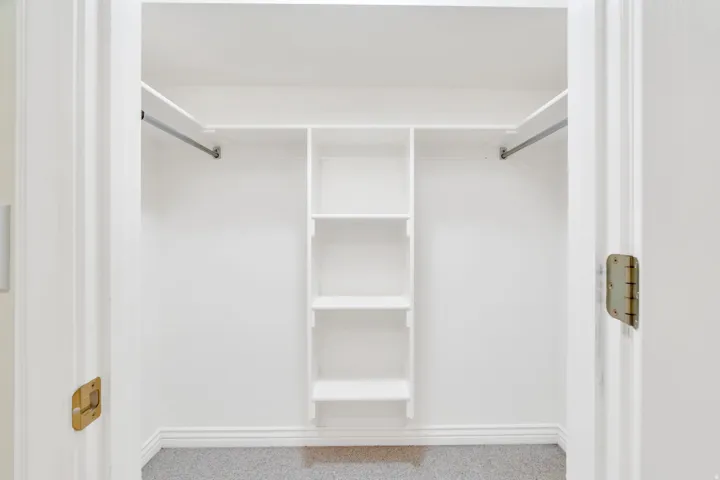 Built-in closet system featuring white shelving, hanging rods, and carpet flooring