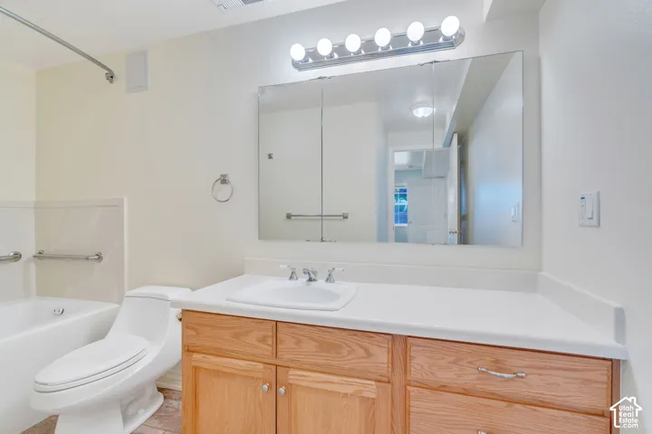 Bathroom featuring a wood-finish vanity with a white countertop and integrated sink, a large wall-mounted mirror, a tub with grab bars, and light wall finishes