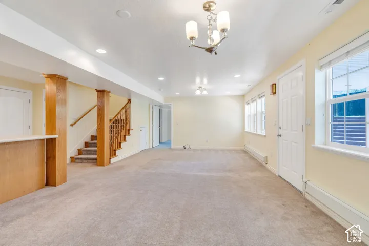 Spacious carpeted room featuring a wood-finish staircase with matching newel posts and handrail, multiple windows, a ceiling-mounted light fixture, and recessed lighting