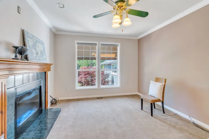 Room featuring a fireplace with a wood mantle and dark tile surround, two windows, carpeted flooring, and crown molding