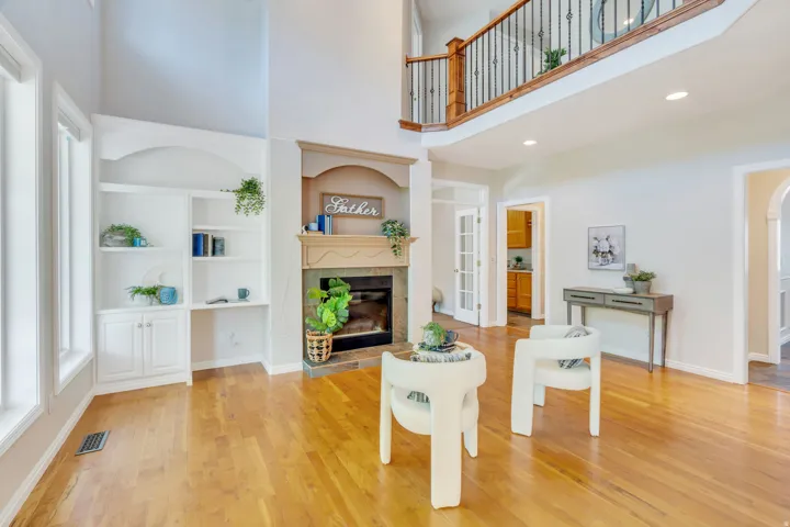 Two-story living area featuring wood-finish flooring, a fireplace with a mantel, built-in shelving, a second-story balcony with metal and wood railings, and white French doors