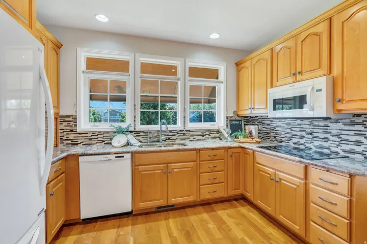 Kitchen featuring light wood cabinetry, stone-finish countertops, a horizontal mosaic tile backsplash, wood-finish flooring, and recessed lighting