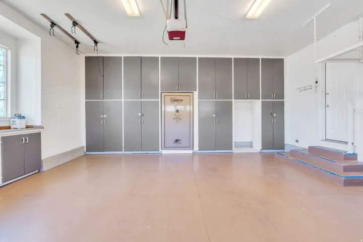 Spacious garage featuring extensive built-in cabinetry, durable flooring, a window, integrated overhead storage racks, and a garage door opener