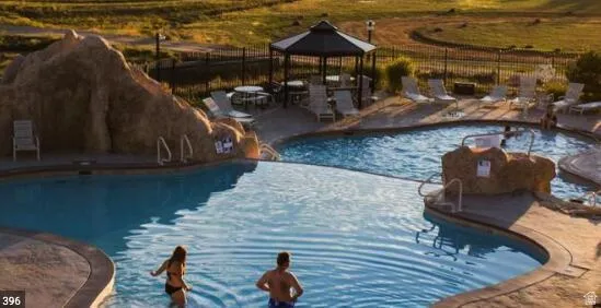 Resort-style aquatic area featuring multiple swimming pools, a rock-detailed grotto, an integrated spa, a shaded gazebo, and extensive lounge seating