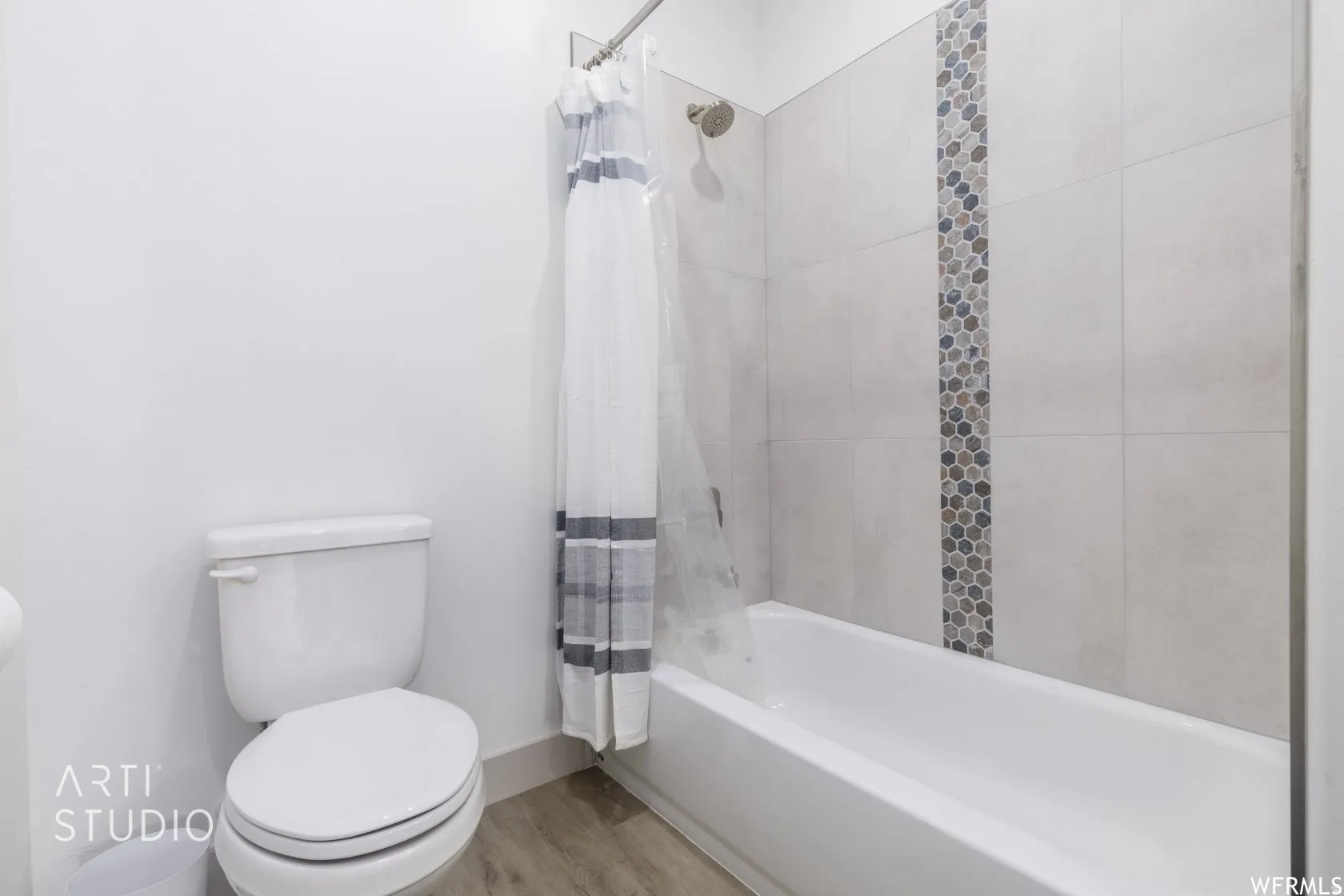 Full bathroom featuring a white tub, light-toned wall tile, decorative mosaic tile accent, and wood-finish flooring