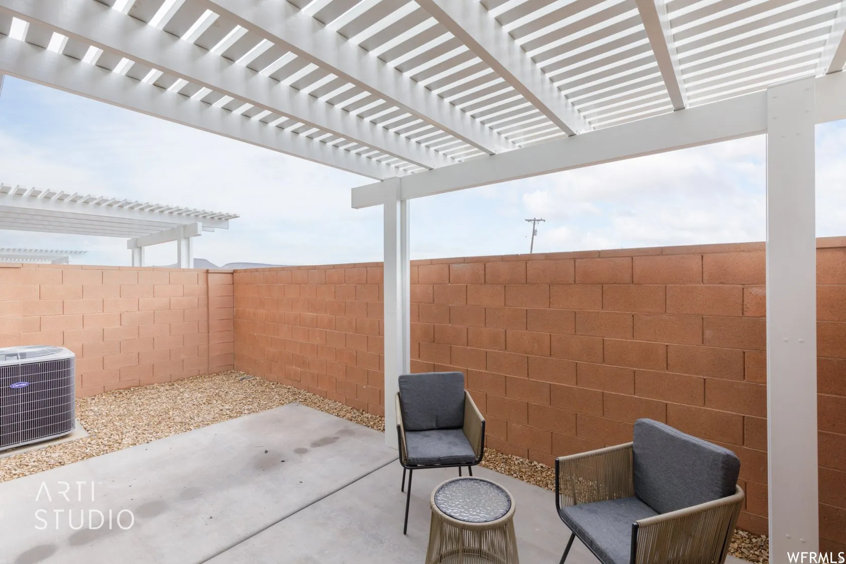 Outdoor patio featuring a white pergola, concrete flooring, and a gravel perimeter