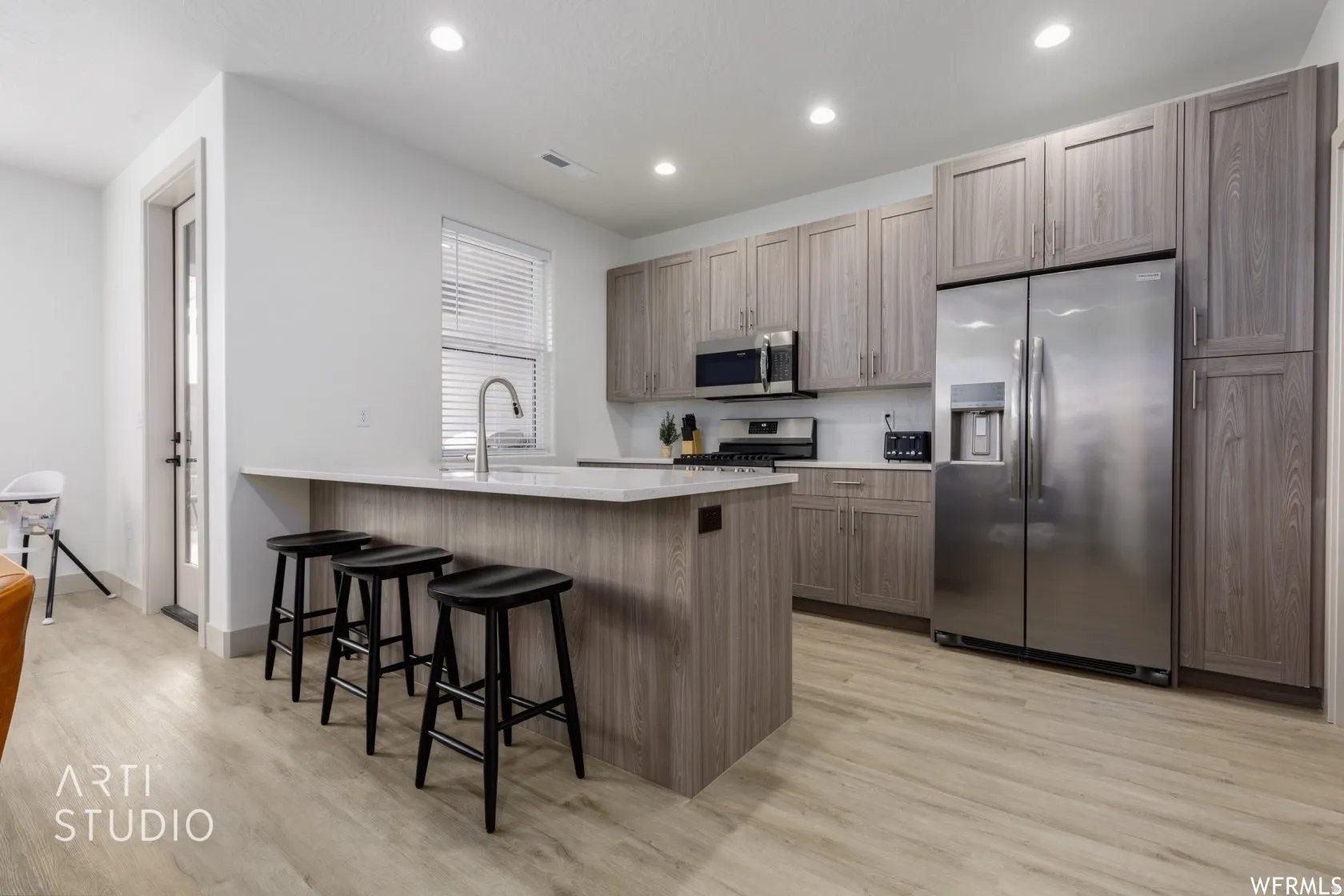 Contemporary kitchen featuring an island with countertop seating, wood-finish flooring, stainless steel appliances, and abundant cabinetry