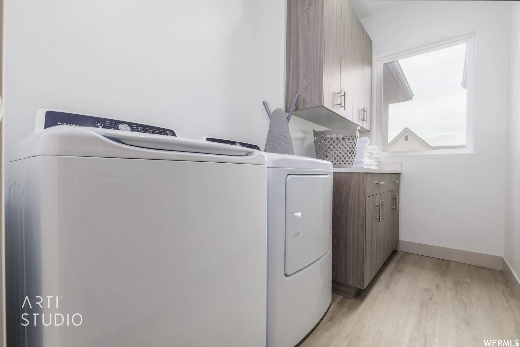 Dedicated laundry area featuring wood-finish flooring, wood-grain cabinetry with brushed nickel hardware, and a window for natural light