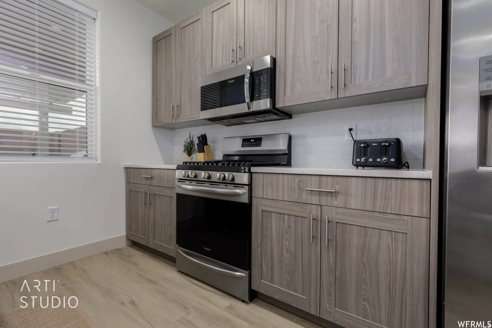 Kitchen featuring light wood-finish cabinetry, stainless steel appliances, a white subway tile backsplash, and light-toned countertops