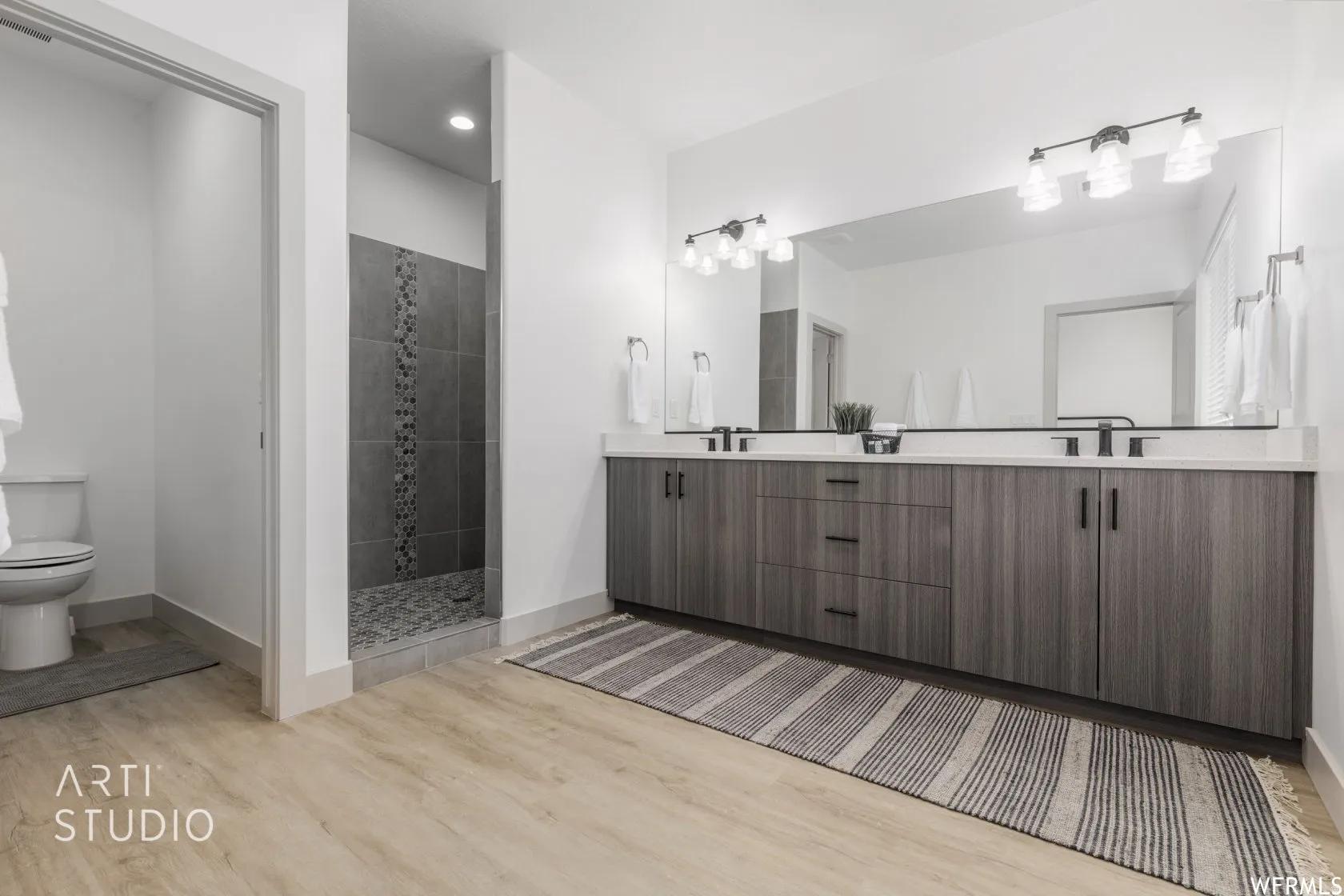 Contemporary bathroom featuring a double vanity with stone countertops, modern wood-finish cabinetry, matte black fixtures, a spacious walk-in shower with stone tile, and light wood-finish flooring