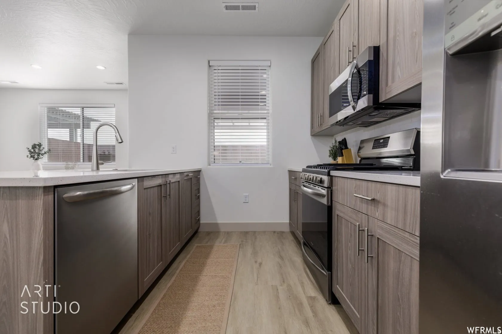Contemporary kitchen featuring wood-finish cabinetry, stainless steel appliances, a gooseneck faucet, light-toned countertops, and wood-finish flooring