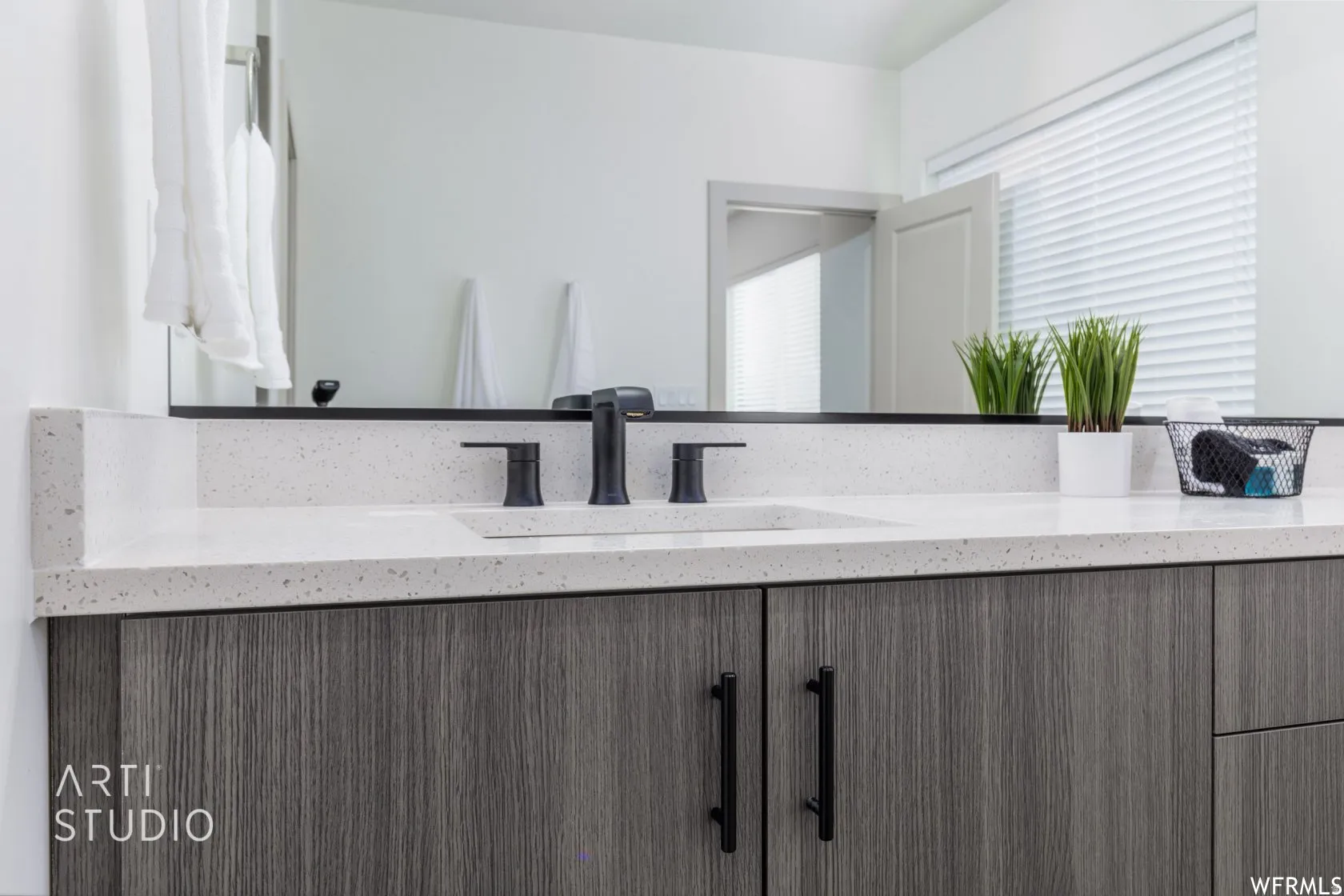 Bathroom vanity featuring a light speckled countertop, integrated rectangular sink, and matte black fixtures