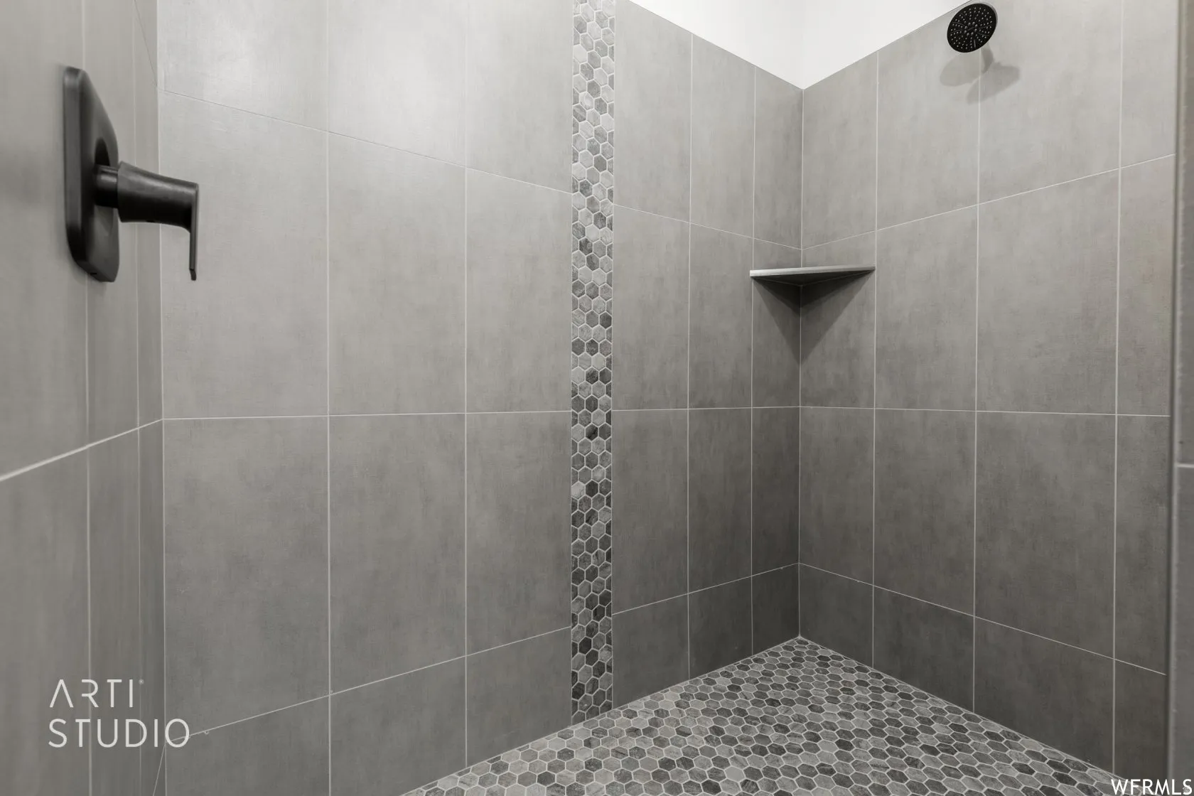 Walk-in shower with large format gray wall tiling, a decorative vertical mosaic accent, a built-in corner shelf, and a dark bronze rainfall showerhead