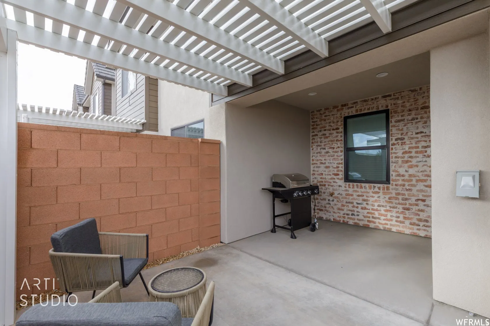 Outdoor patio featuring a white pergola, concrete flooring, and a brick accent wall