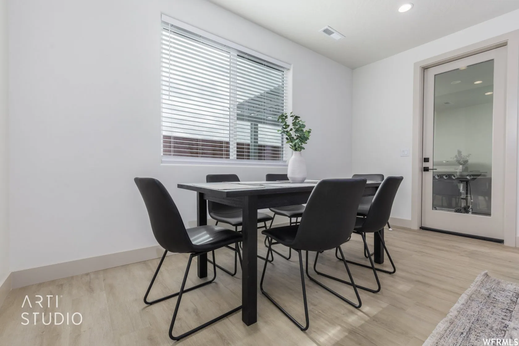 Dining area featuring wood-finish flooring, a large window with blinds, and a light-colored full-glass paneled door