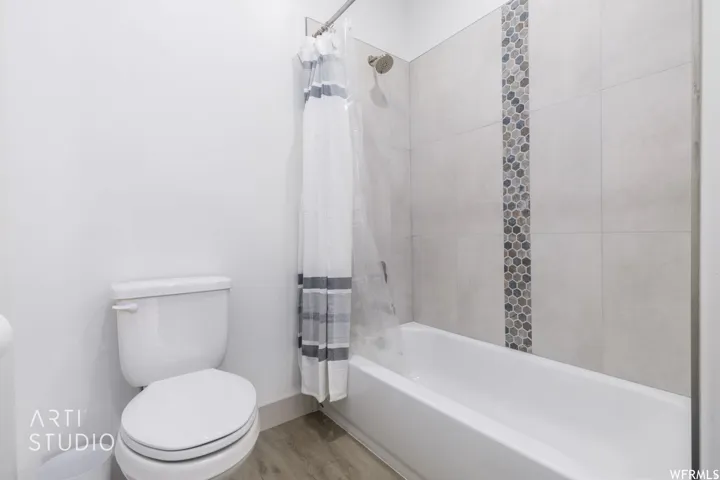 Full bathroom featuring a white tub, light-toned wall tile, decorative mosaic tile accent, and wood-finish flooring