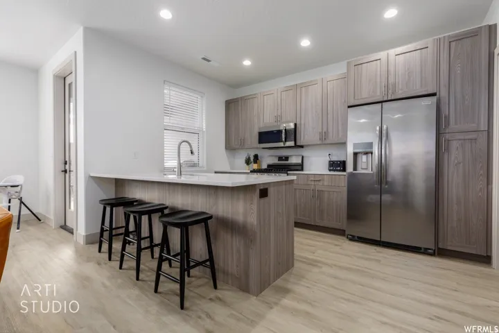 Contemporary kitchen featuring an island with countertop seating, wood-finish flooring, stainless steel appliances, and abundant cabinetry