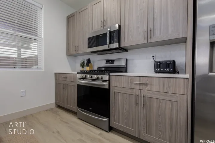 Kitchen featuring light wood-finish cabinetry, stainless steel appliances, a white subway tile backsplash, and light-toned countertops