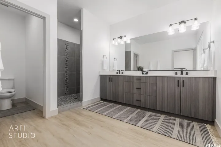 Contemporary bathroom featuring a double vanity with stone countertops, modern wood-finish cabinetry, matte black fixtures, a spacious walk-in shower with stone tile, and light wood-finish flooring