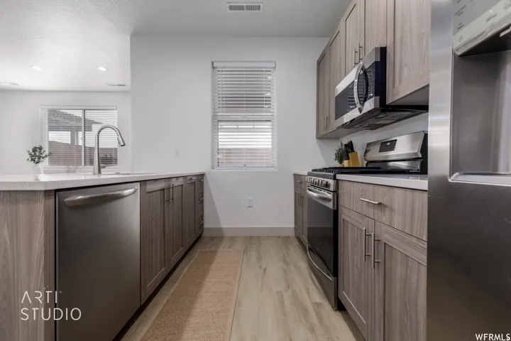 Contemporary kitchen featuring wood-finish cabinetry, stainless steel appliances, a gooseneck faucet, light-toned countertops, and wood-finish flooring