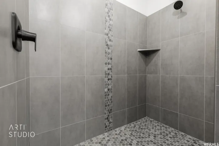 Walk-in shower with large format gray wall tiling, a decorative vertical mosaic accent, a built-in corner shelf, and a dark bronze rainfall showerhead