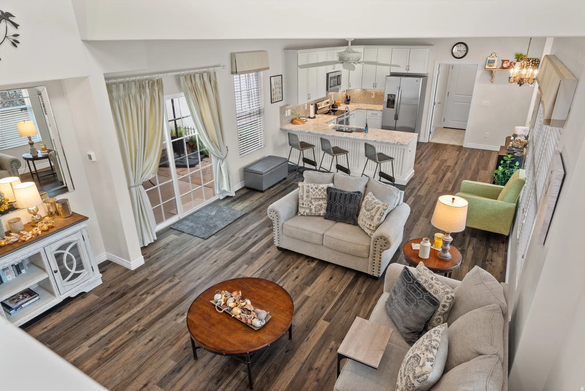 Open-concept living space featuring wood-finish flooring, a white kitchen with stainless steel appliances, and a breakfast bar