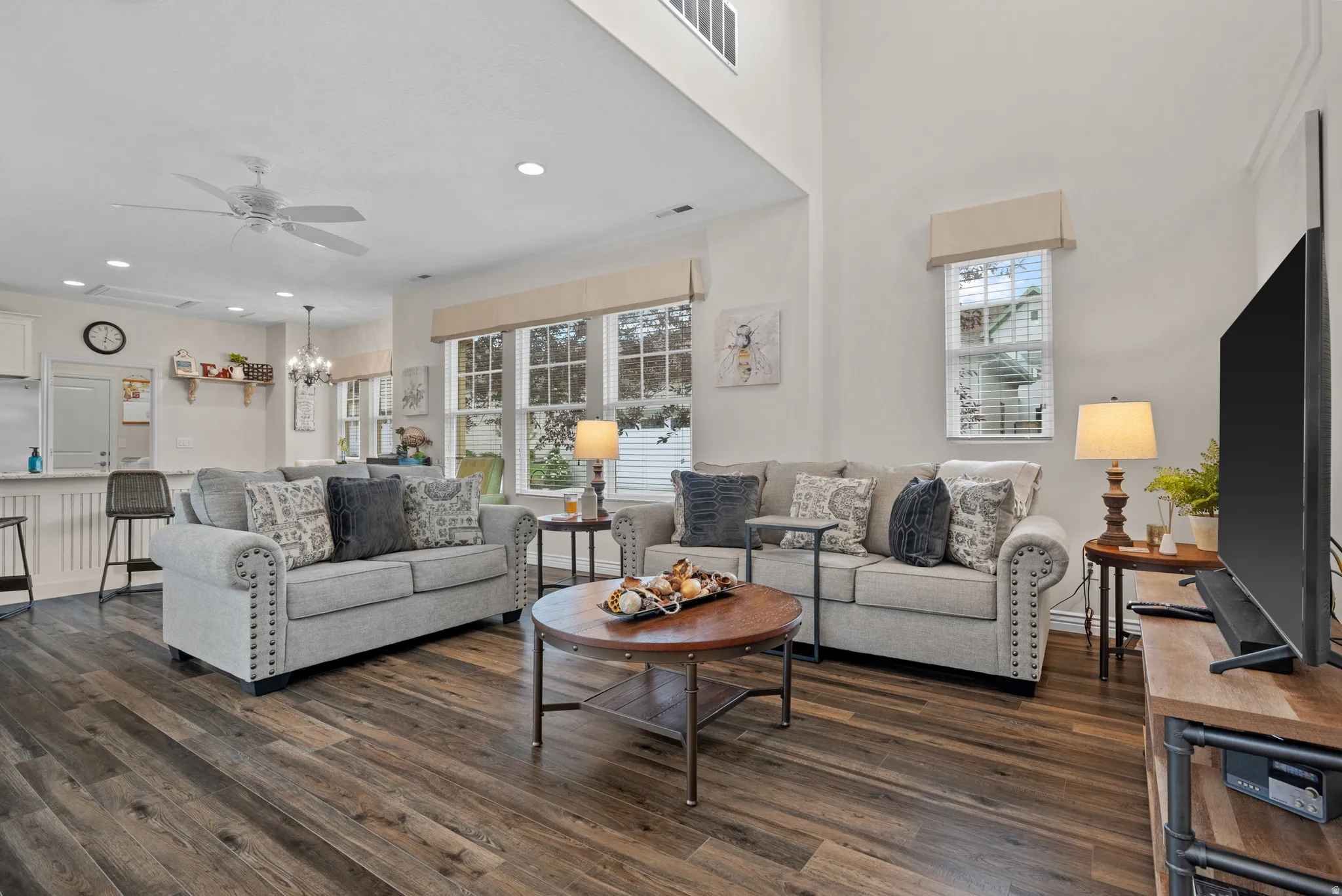 Open-concept living space featuring wood-finish flooring, high ceilings, multiple windows with blinds, recessed lighting, and a ceiling fan