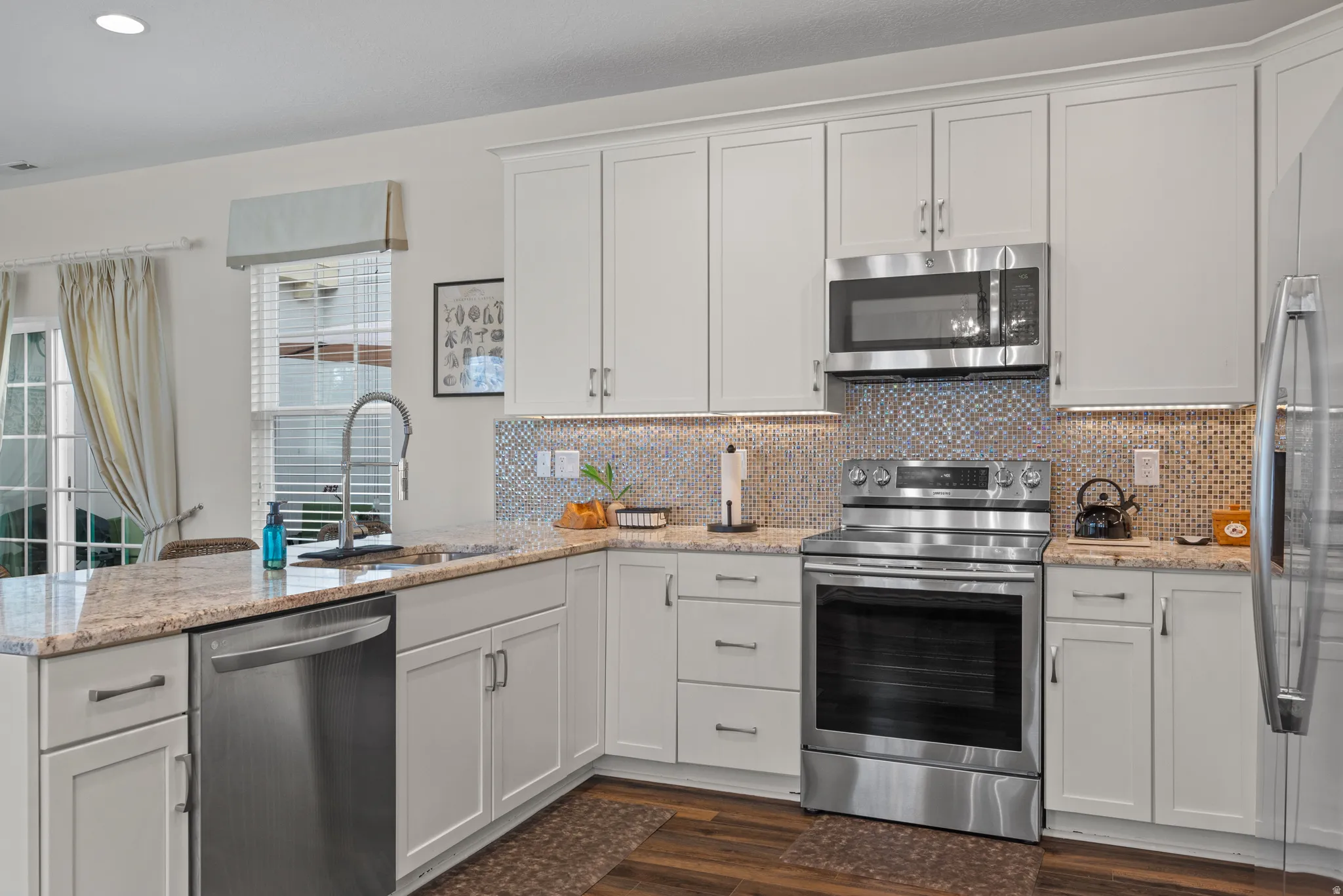 Modern kitchen featuring white shaker cabinetry, stainless steel appliances, speckled countertops, and a mosaic tile backsplash