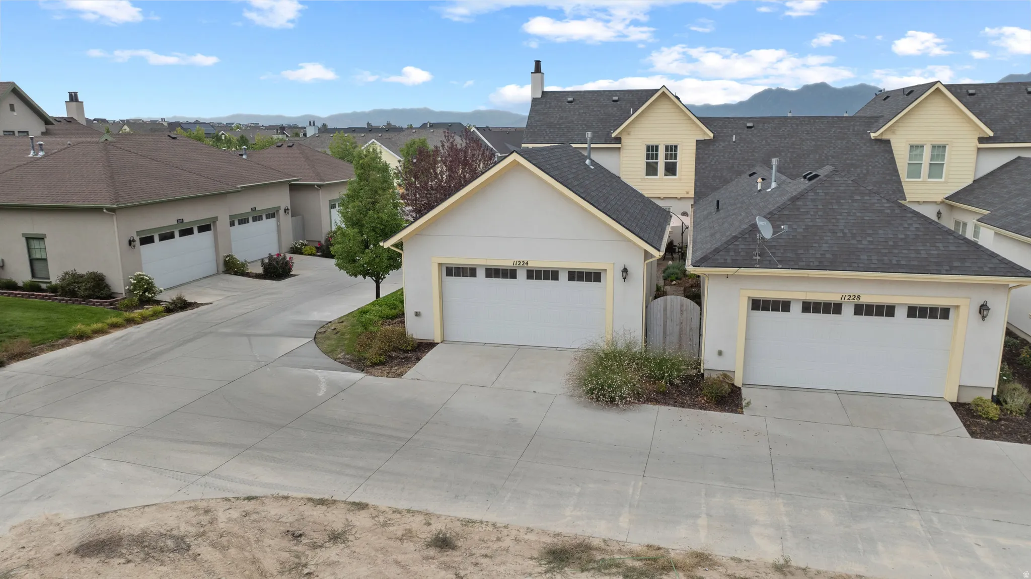 Residential streetscape featuring multiple garages with white sectional doors, light stucco siding, and dark shingle roofs