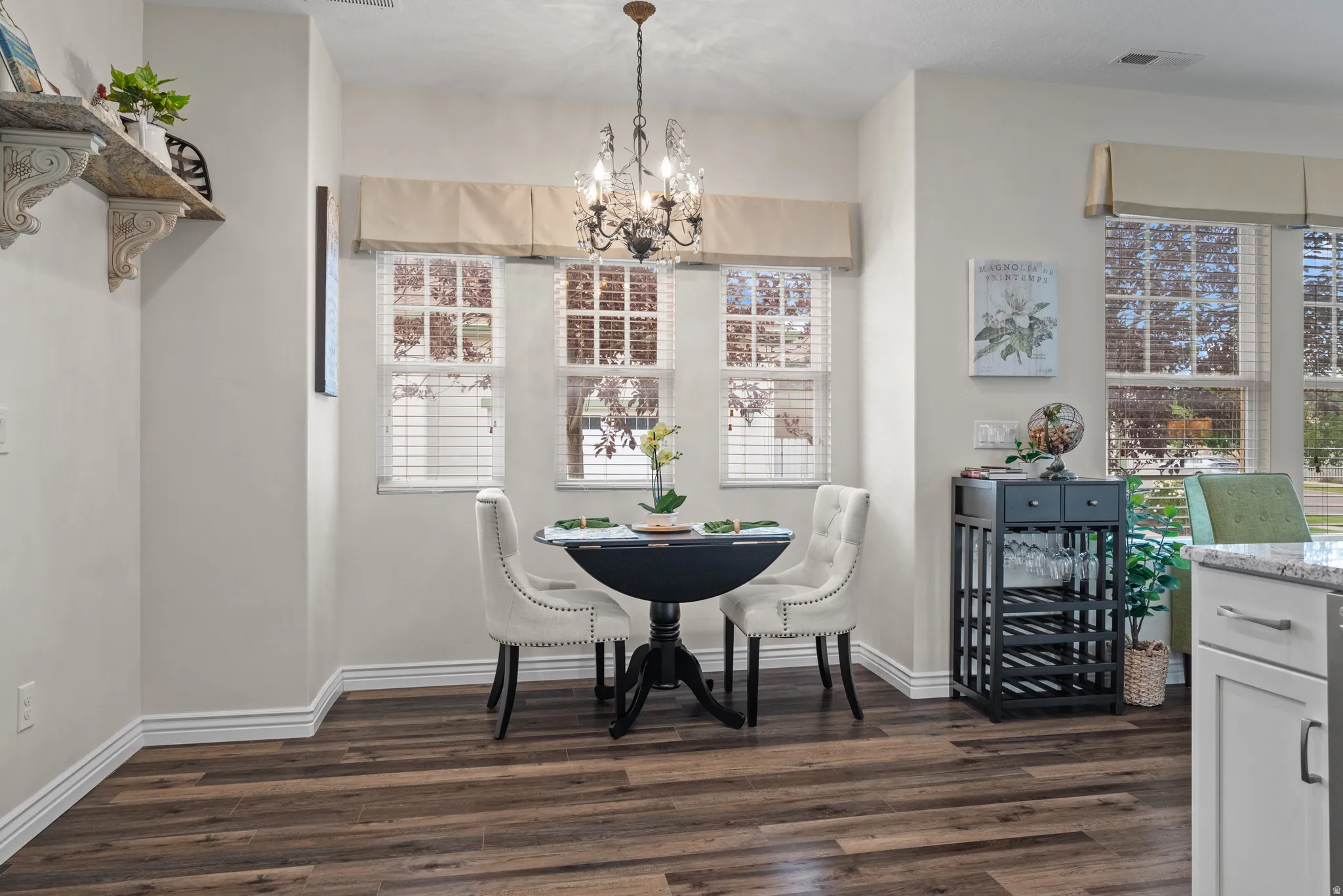 Dining area featuring wood-finish flooring, a decorative chandelier, multiple windows with blinds, a built-in shelving unit, and a stone-finish countertop
