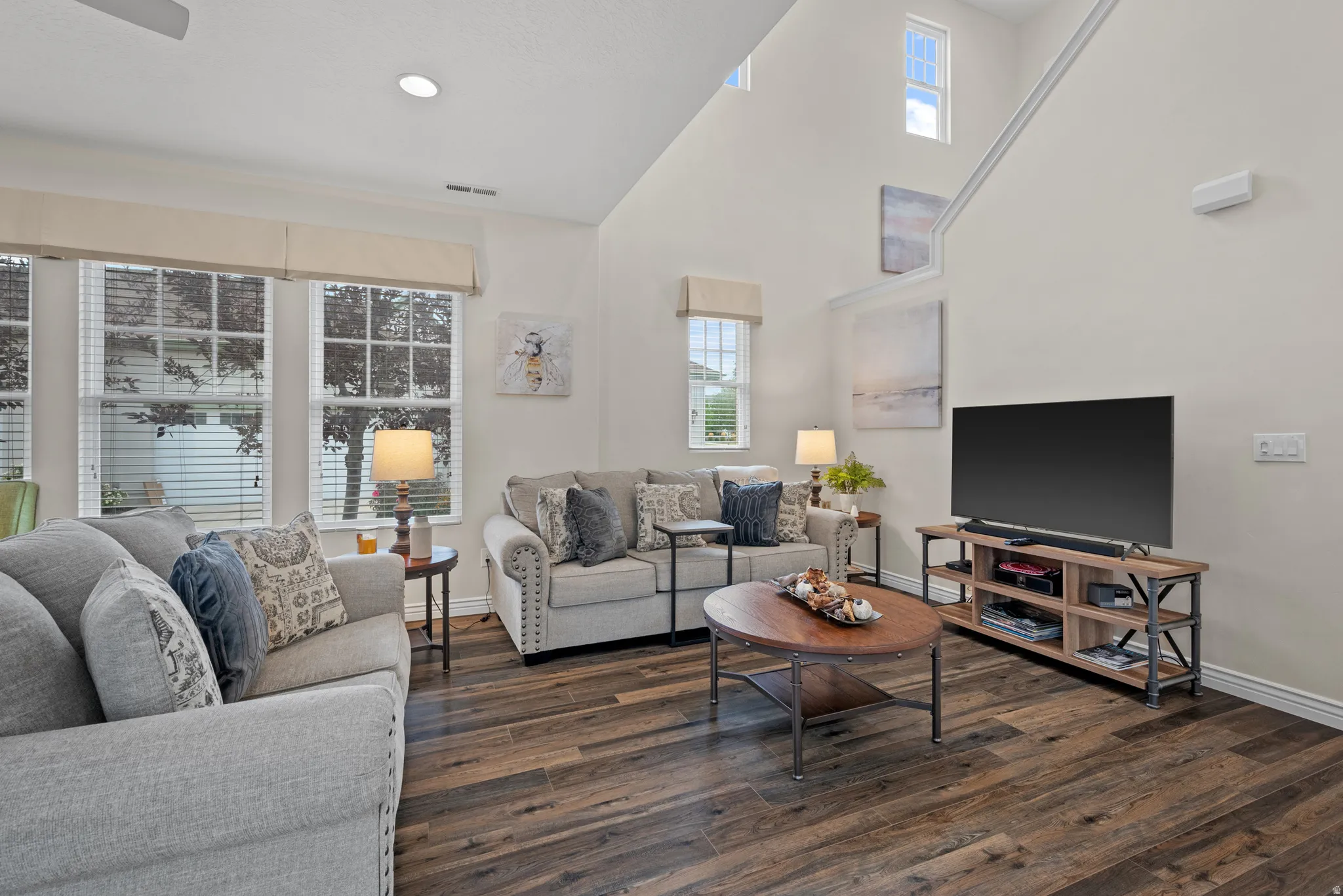 Vaulted living space featuring wood-finish flooring, multiple windows with blinds, and white baseboards