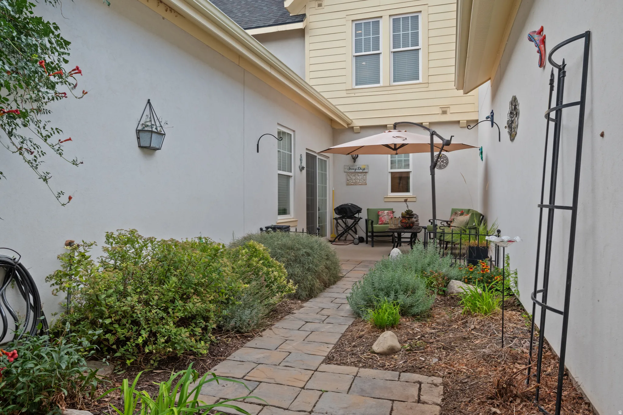 Private patio space featuring a paved walkway, established garden beds, and direct access to interior via sliding glass door