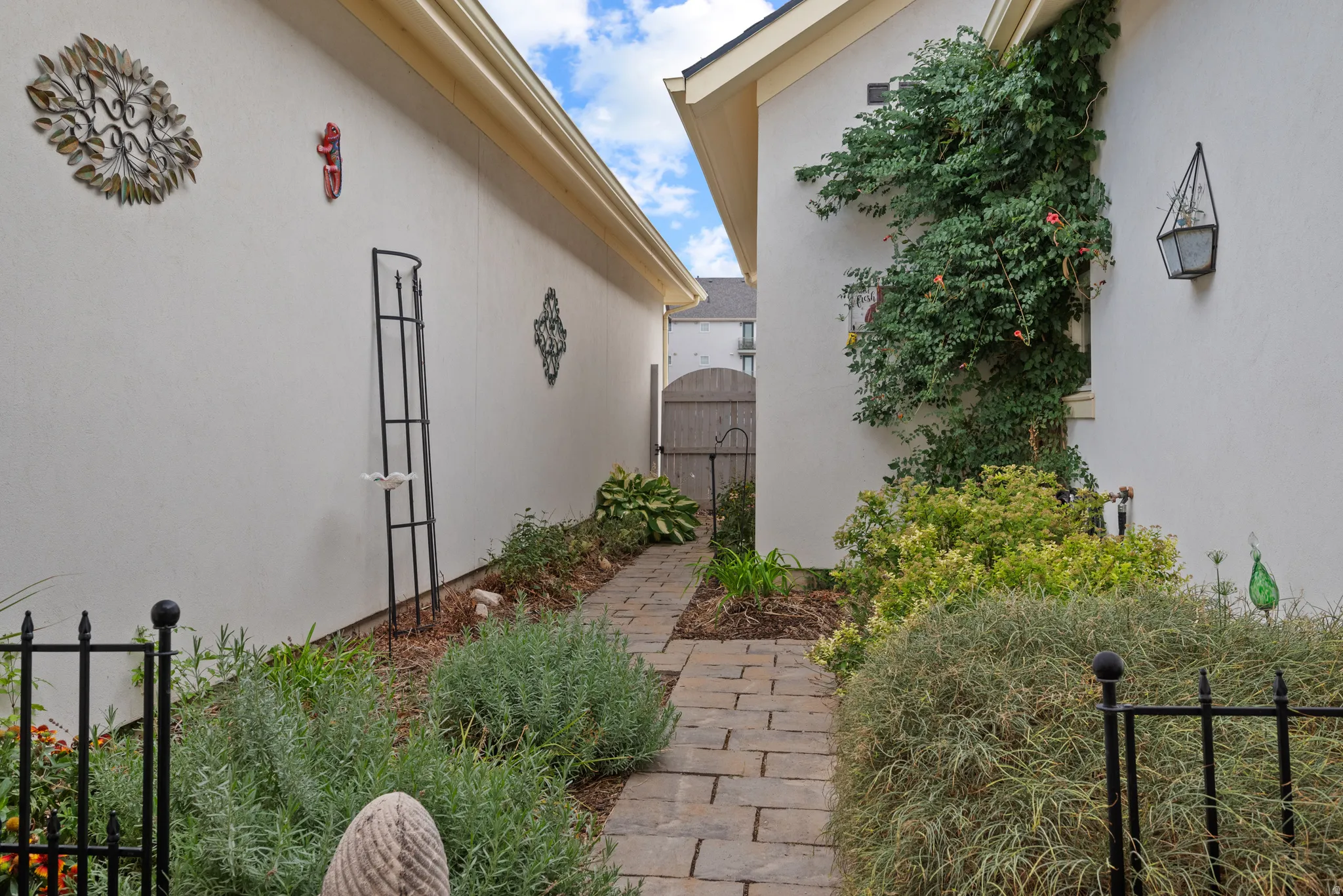Stone paver pathway bordered by established landscaping and stucco walls, featuring a decorative privacy gate
