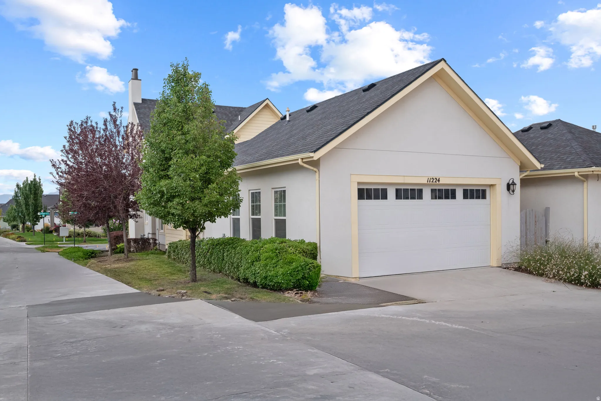 Single-story residence featuring a two-car garage with transom windows, light stucco exterior, and a dark shingle roof