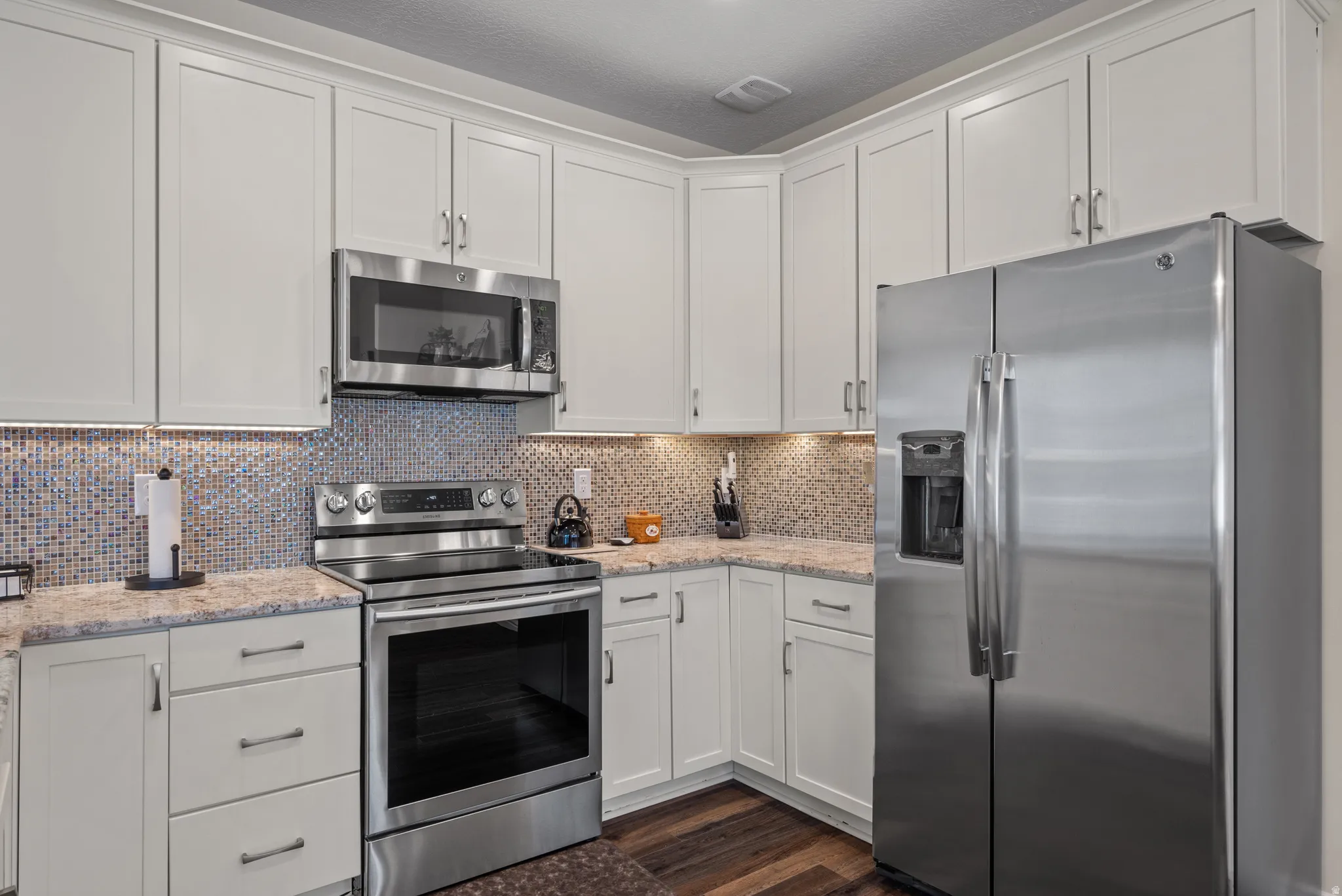 Contemporary kitchen featuring white cabinetry, stainless steel appliances, a mosaic tile backsplash, under-cabinet lighting, and wood-finish flooring