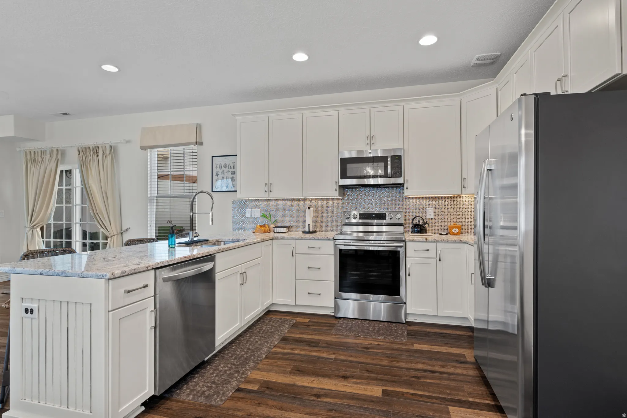 Modern kitchen featuring white cabinetry, wood-finish flooring, stainless steel appliances, a mosaic tile backsplash, and a light-toned countertop with an integrated sink